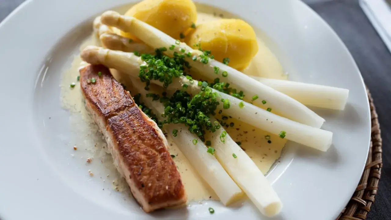 Ein Stück Lachs mit Spargel, Kartoffeln und Sauce Hollandaise. Der Spargel ist mit Schnittlauch bestreut.