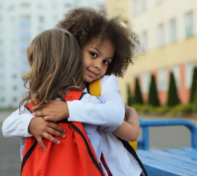 Zwei Kinder umarmen sich. Ein Mädchen mit Locken lächelt in die Kamera. Ein schönes Beispiel für Empathie bei Kindern.