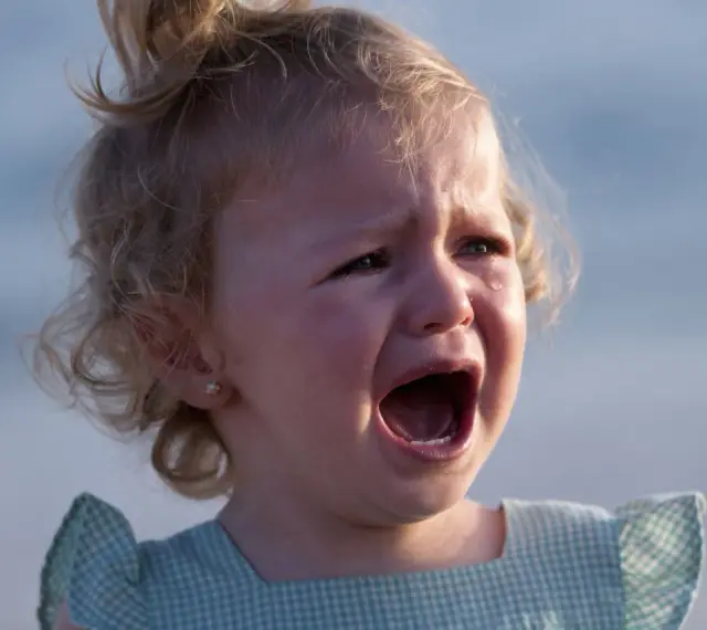 Ein kleines Mädchen mit blonden Locken weint bitterlich. Tränen laufen über ihre Wangen. Wahrscheinlich ist sie mitten in der Trotzphase mit 2 Jahren.