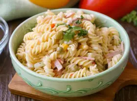 Schüssel mit cremigem Nudelsalat, garniert mit Petersilie. Darin Fusilli-Nudeln, Erbsen, Mais und Schinkenwürfel – ein leckerer Nudelsalat mit Fleischsalat.