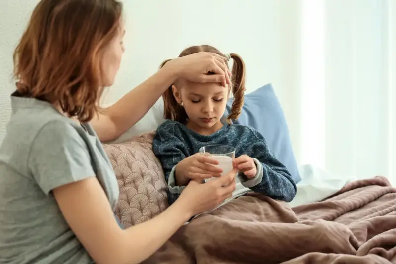 Mutter prüft Fieber bei krankem Kind im Bett. Die Krankschreibung für die Schule ist nötig, damit das Kind sich erholen kann.