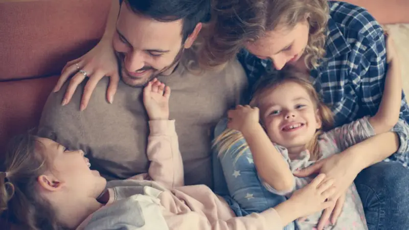 Glückliche Familie kuschelt auf dem Sofa. Zwei Elternteile umarmen ihre zwei Kinder, die sich an sie schmiegen.